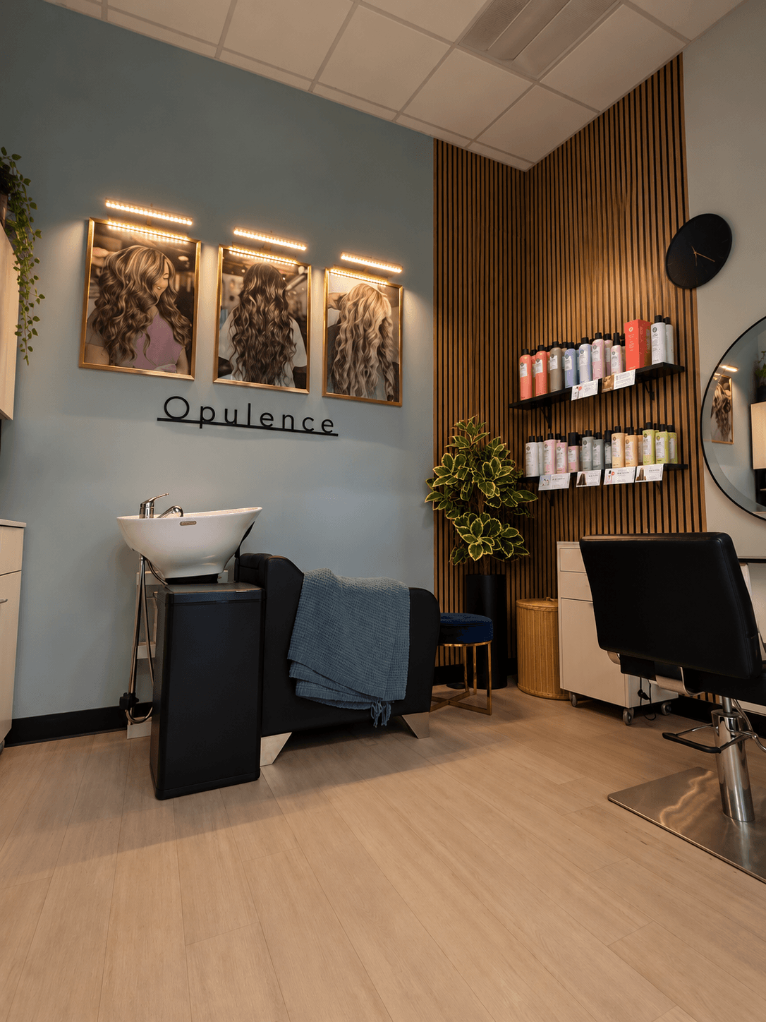 Salon interior with hair washing station, shelves of hair products, a mirror, and a chair, decorated with artwork and lighting.