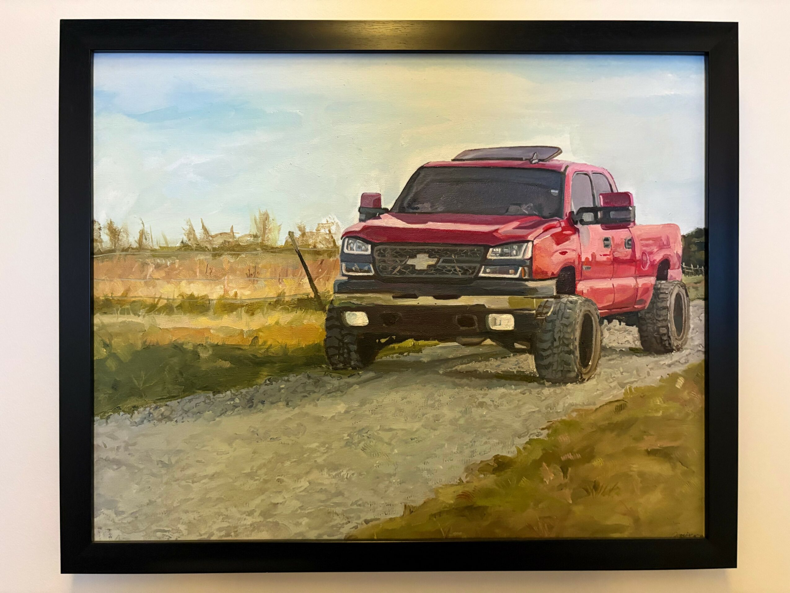 Red pickup truck driving on a dirt road in a rural landscape with a cloudy sky.