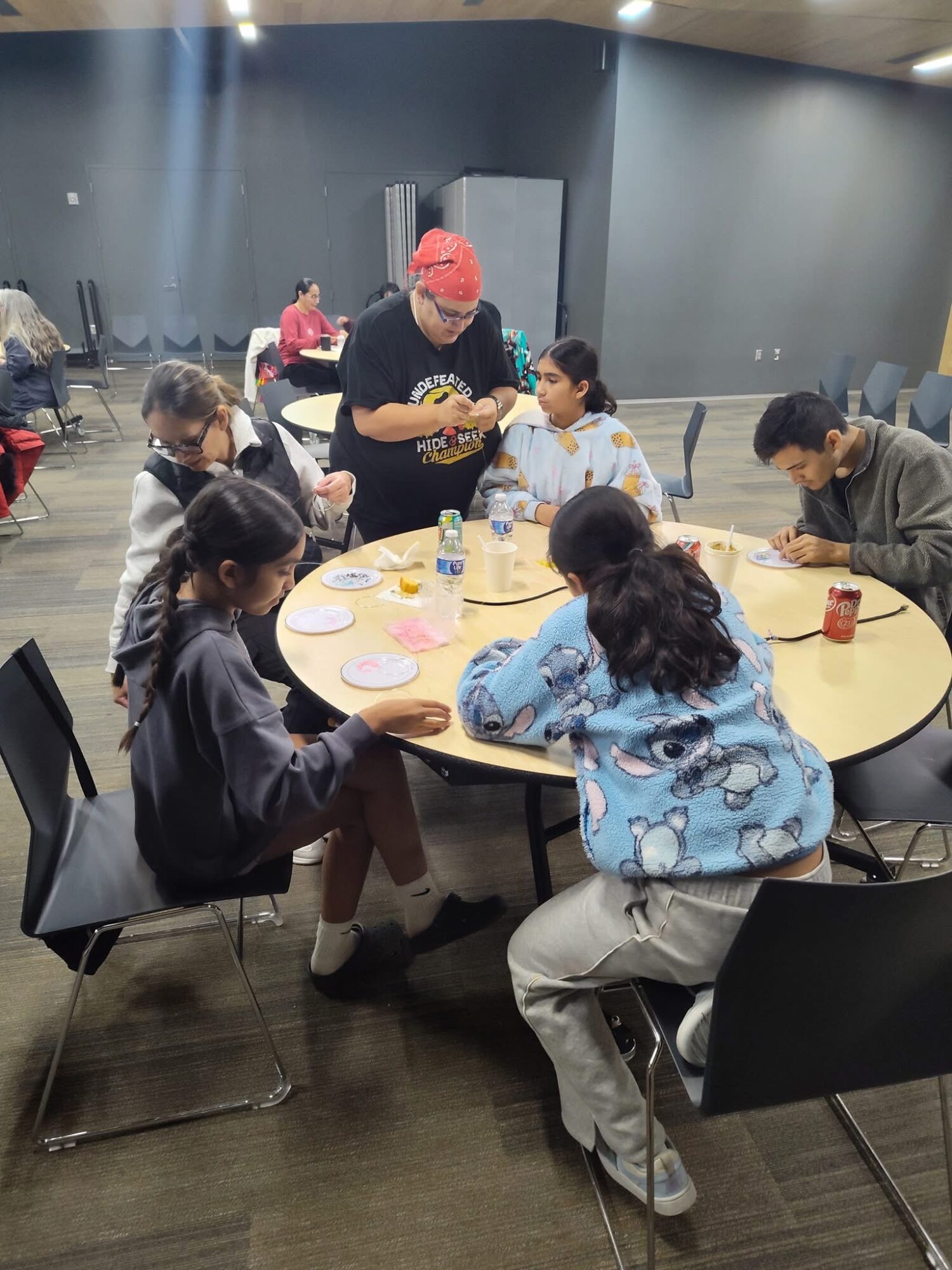 Group of children and an adult around a table with craft supplies in a room with gray walls.
