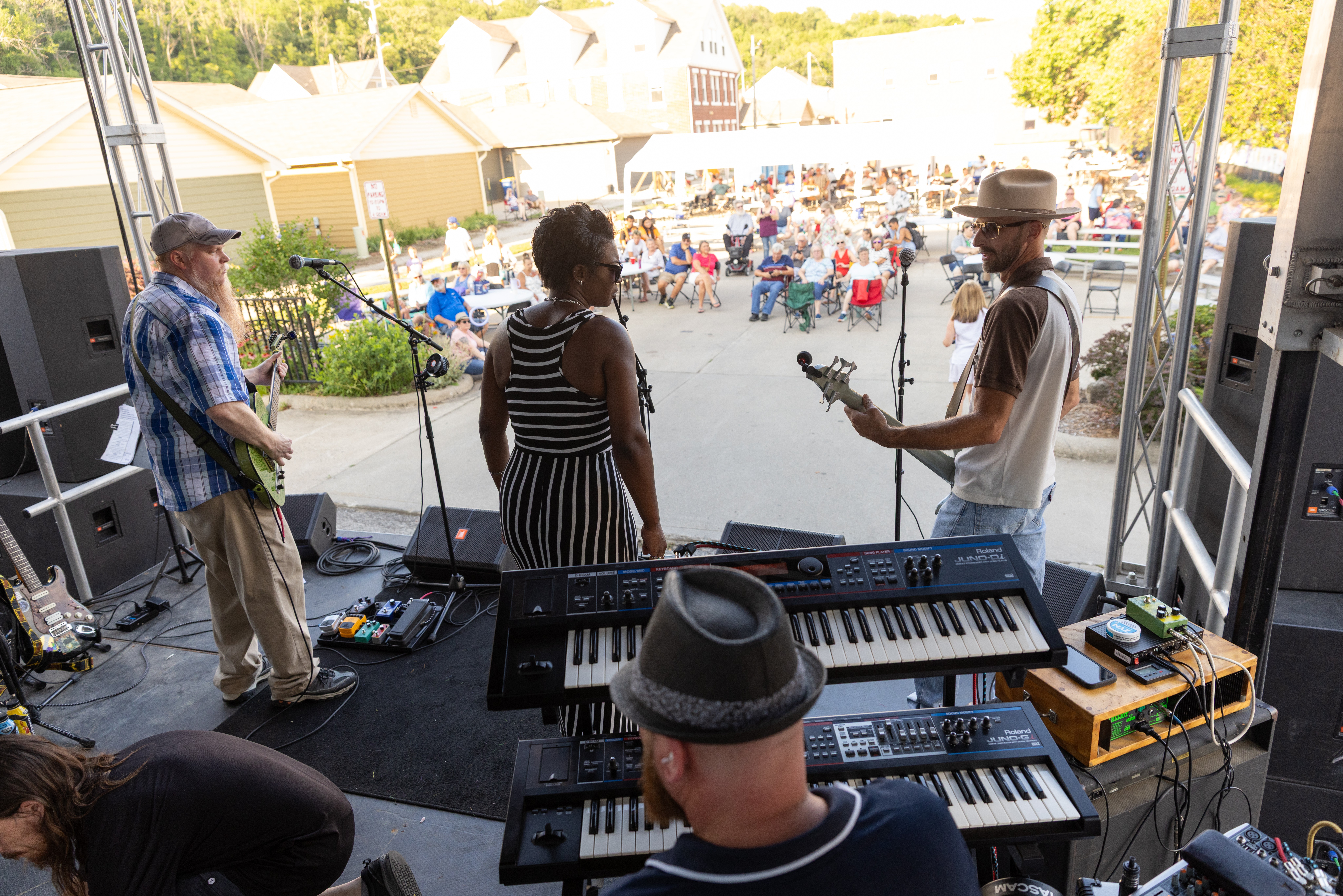 Band performing on stage with three musicians, one playing guitar, one on keyboard, and one on bass, in front of an outdoor audience.