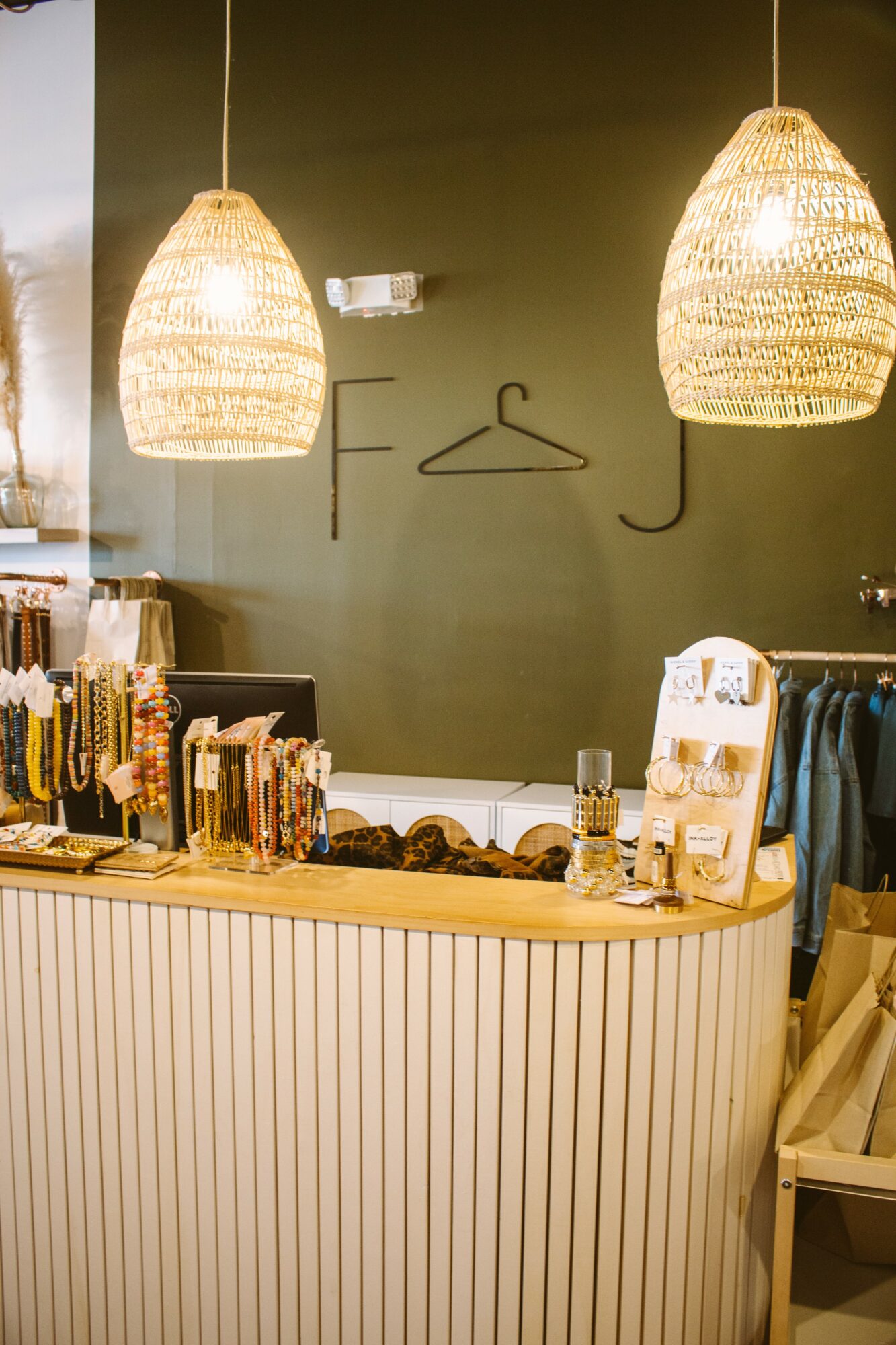 Interior of a shop with hanging woven pendant lights, a green wall, and a counter with books and accessories.