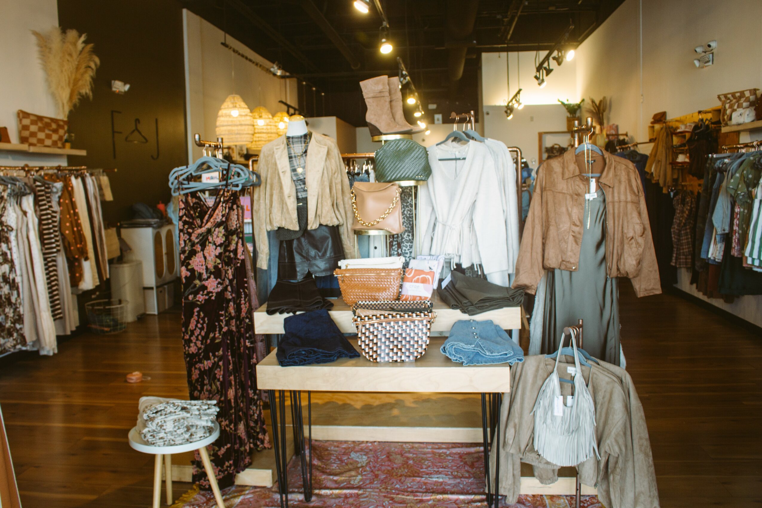 Clothing store interior with mannequins dressed in jackets and pants, shelves with folded clothes, and racks of garments.