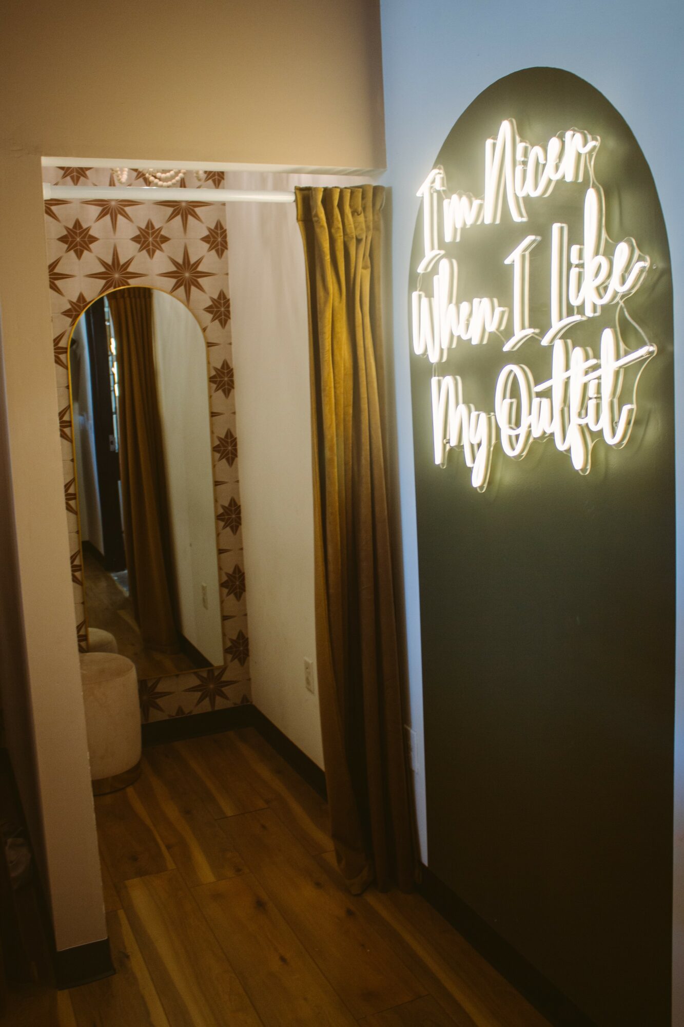 Decorative mirror with floral pattern, yellow curtain, and illuminated sign with text, in a cozy interior space.