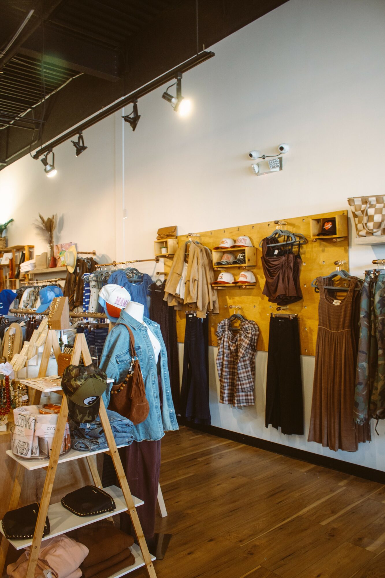 Clothing and accessories displayed on wall and shelves in a retail store interior, with a mannequin and wooden flooring.