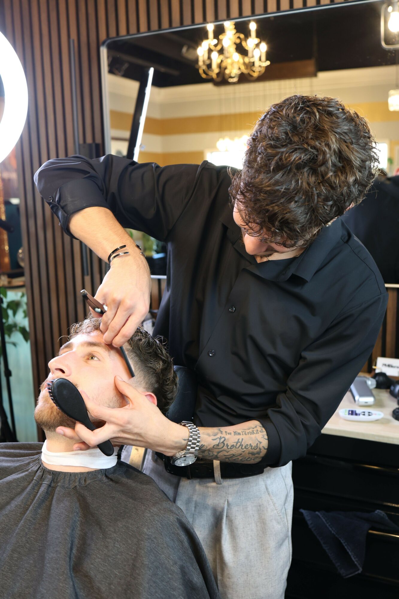 Two women face each other, one applying makeup to the other's face in a salon or studio setting.