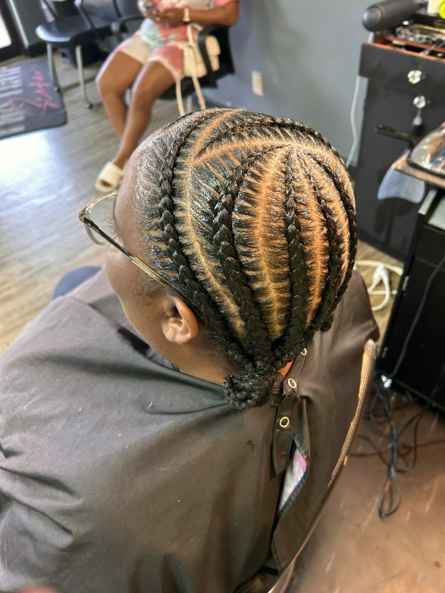 Person with braided hairstyle featuring cornrows and blonde highlights, viewed from above, sitting in a salon chair.