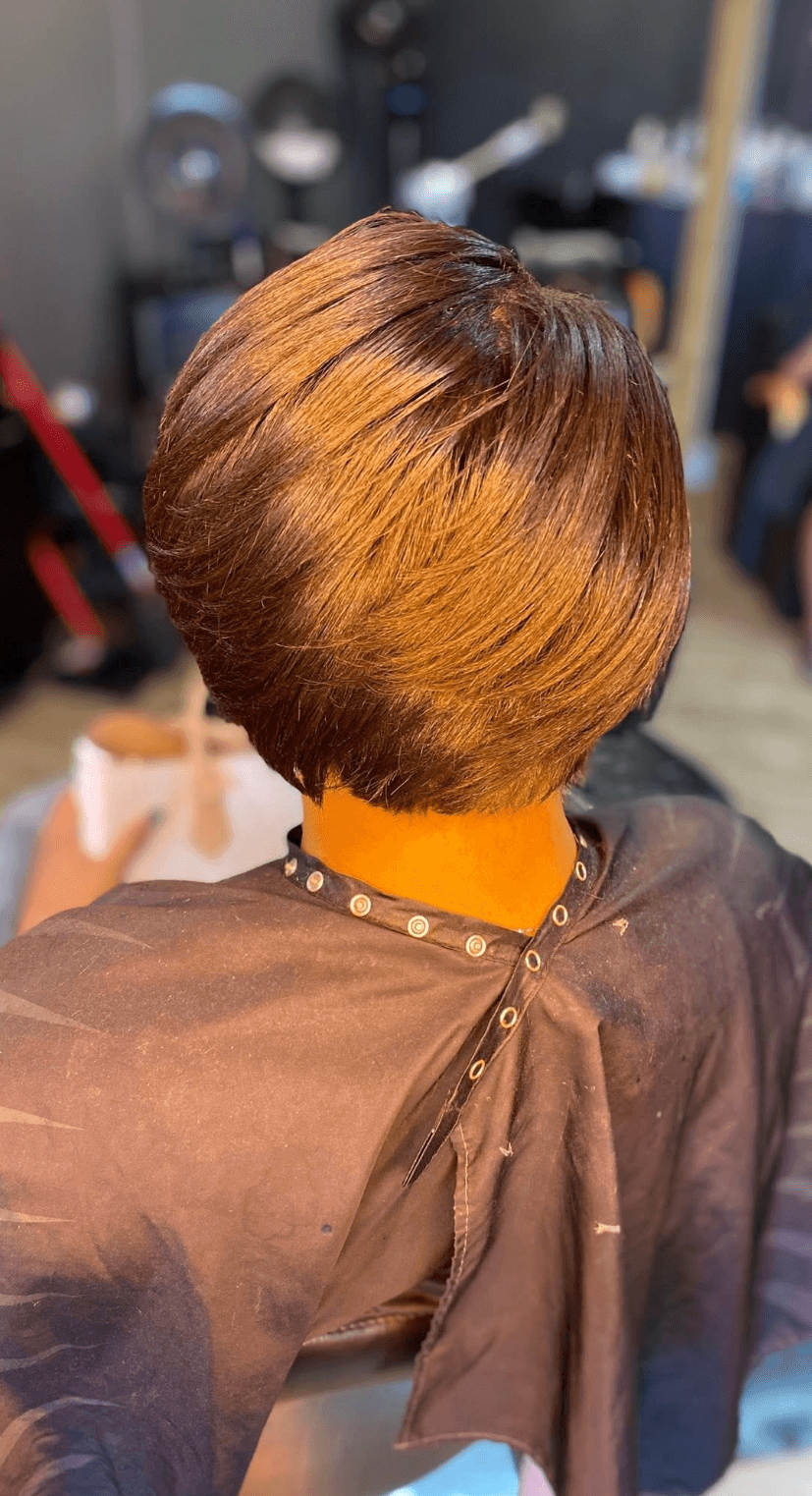 Back view of a person with a short, layered hairstyle in a salon, wearing a dark cape and yellow collar.