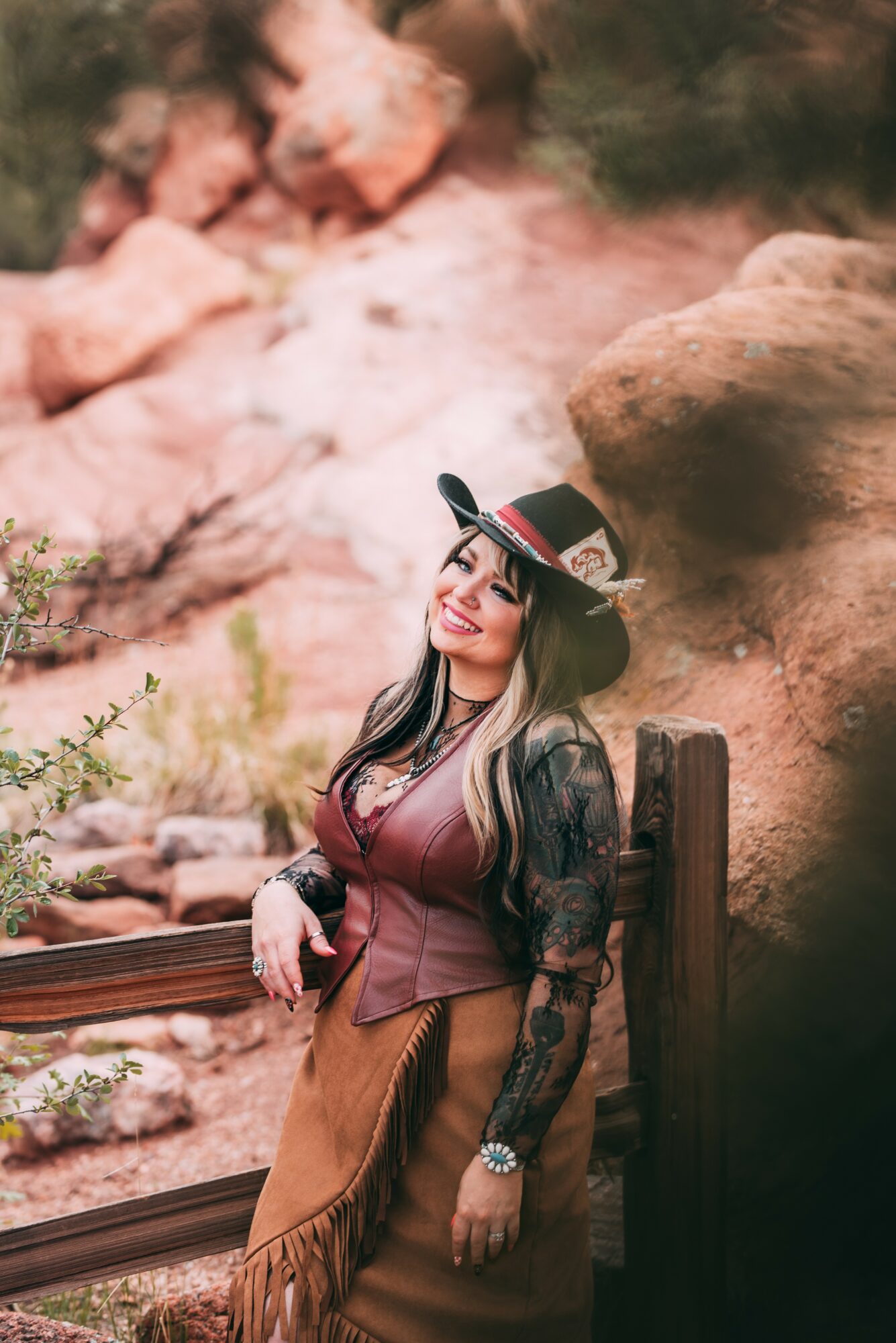 Woman in bohemian outfit and hat standing outdoors with rocks and plants in background.