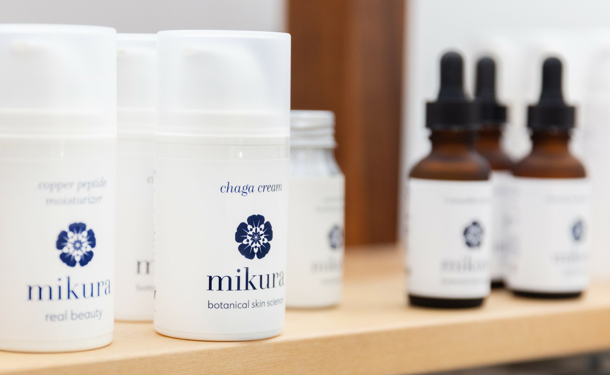 Skincare products on a shelf, including bottles labeled 'mikuna' and small dropper bottles, with a wooden background.