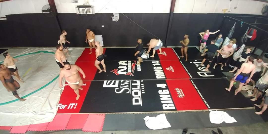 People practicing martial arts or wrestling in a gym with mats and banners on the walls.