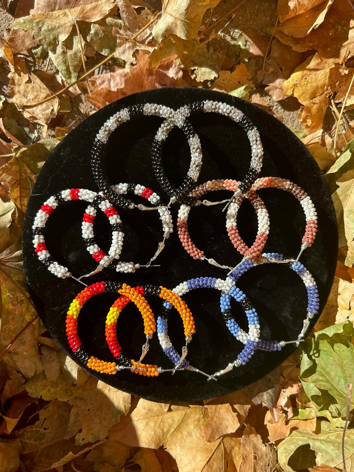 Colorful beaded bracelets arranged in a circle on a black surface, surrounded by autumn leaves.