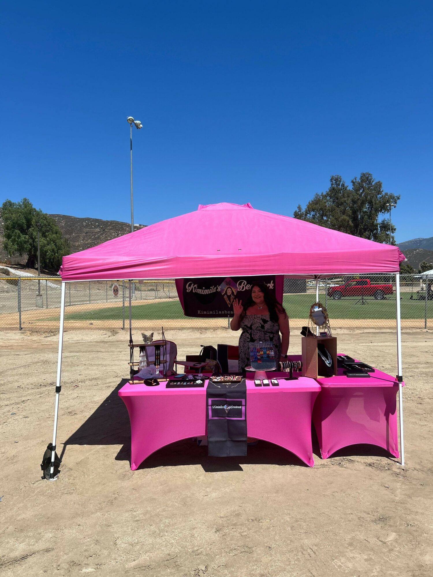 Pink canopy tent with table and chairs outdoors on a sunny day, with trees and a clear blue sky in the background.