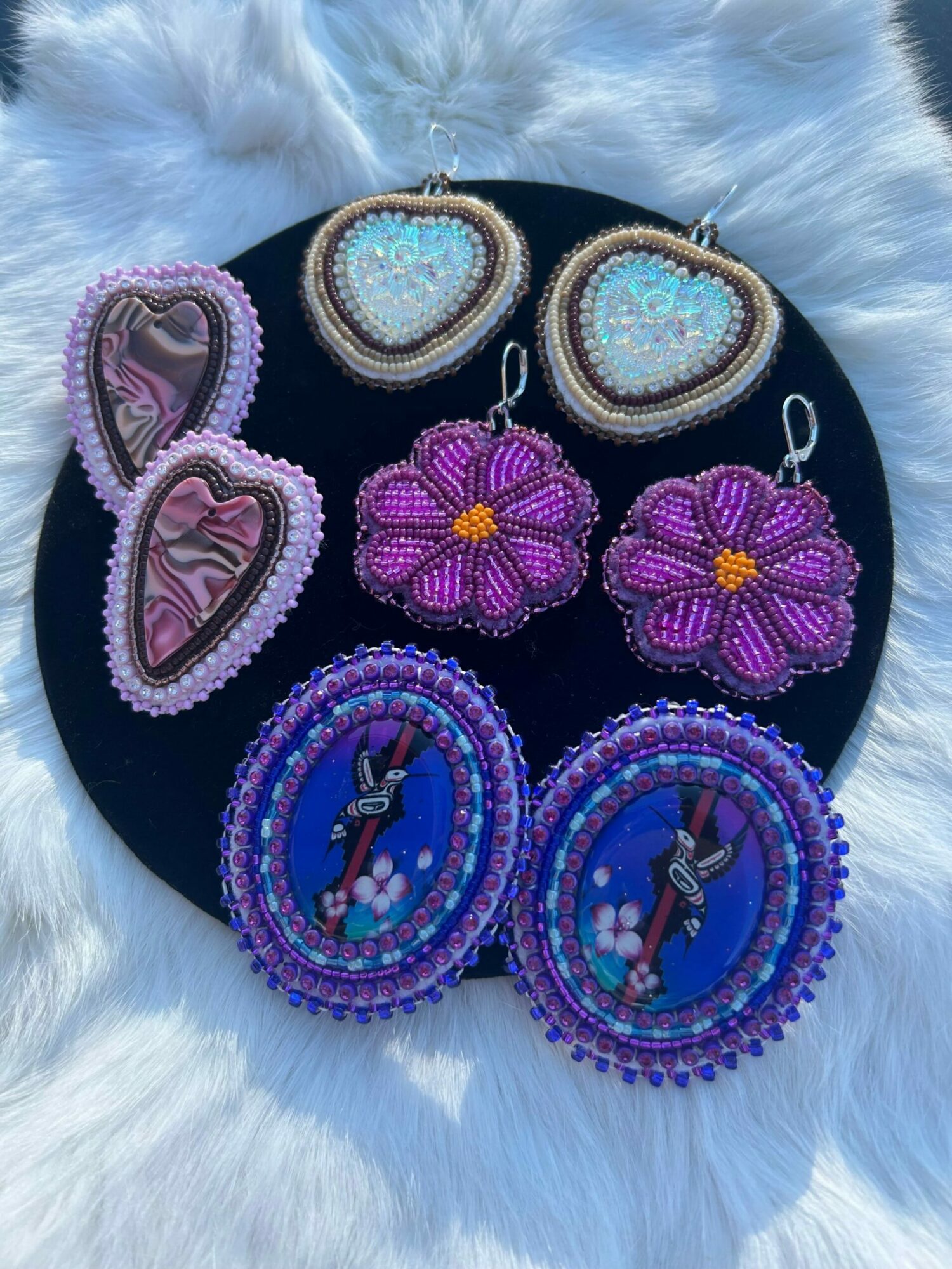 Beaded jewelry and accessories on a black circular display, including purple flowers, teardrop-shaped pieces, and circular items with blue and purple beads.