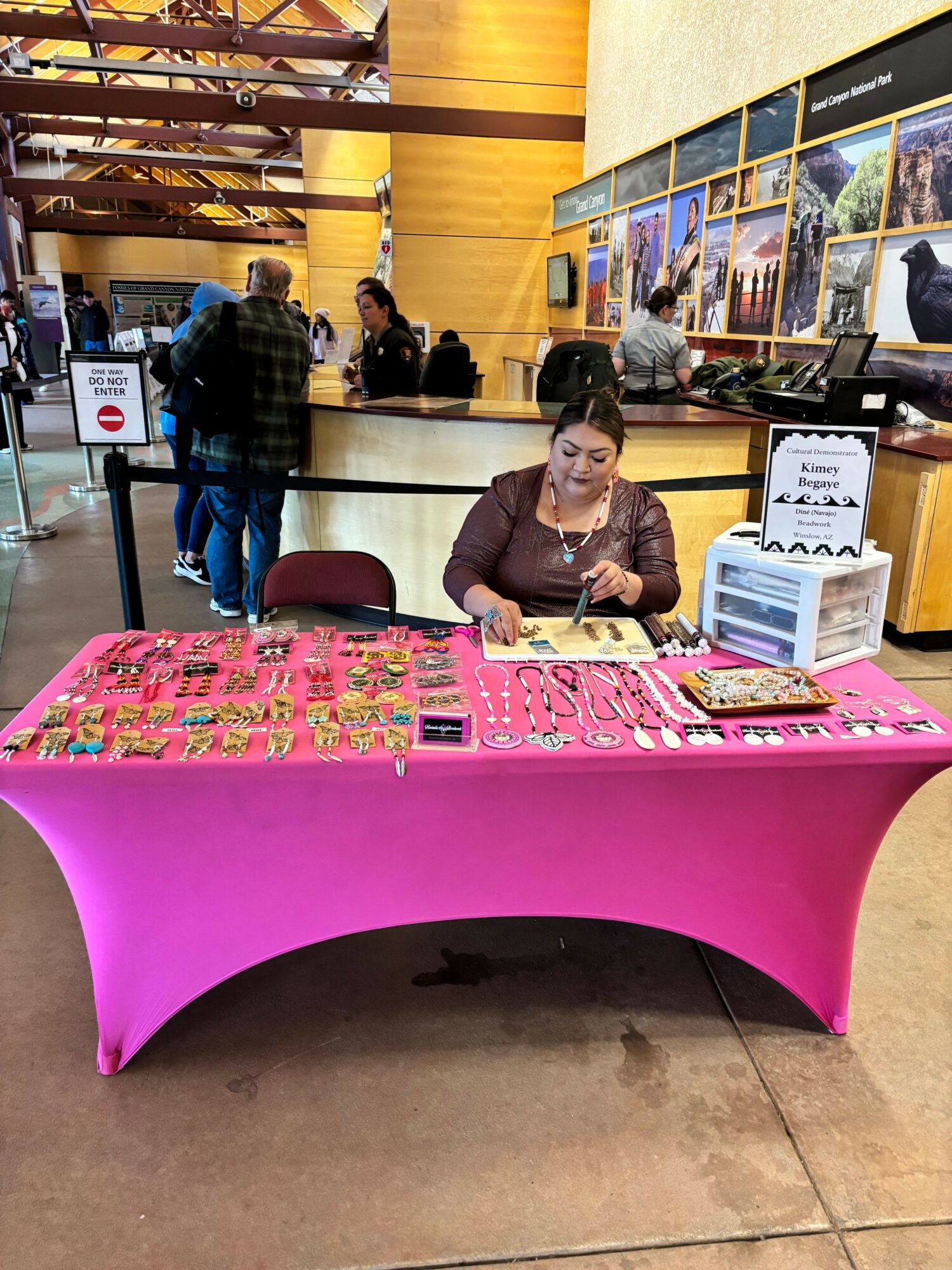 Woman sitting behind a pink table with various items, in an indoor setting with posters on the wall.