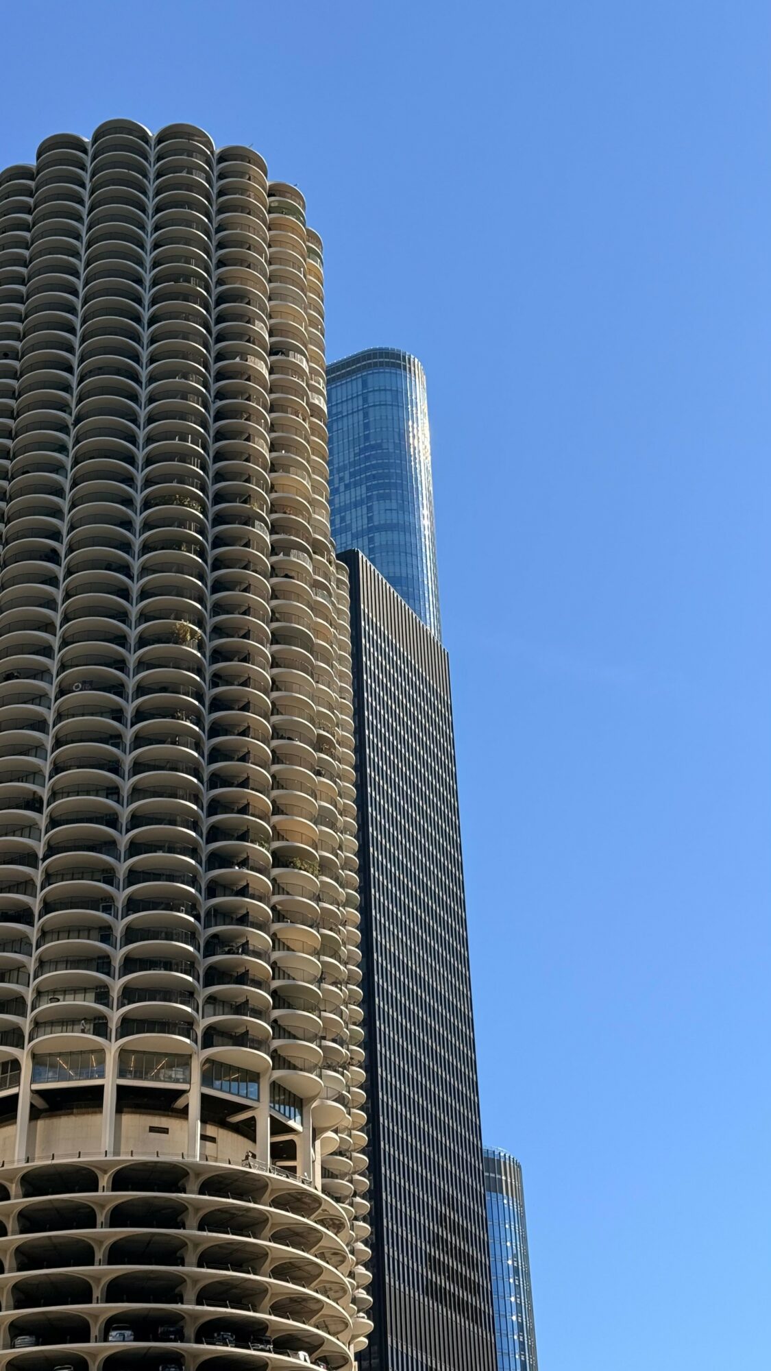 Three tall skyscrapers against a clear blue sky, with one building having a rounded, textured facade and another with a glass exterior.