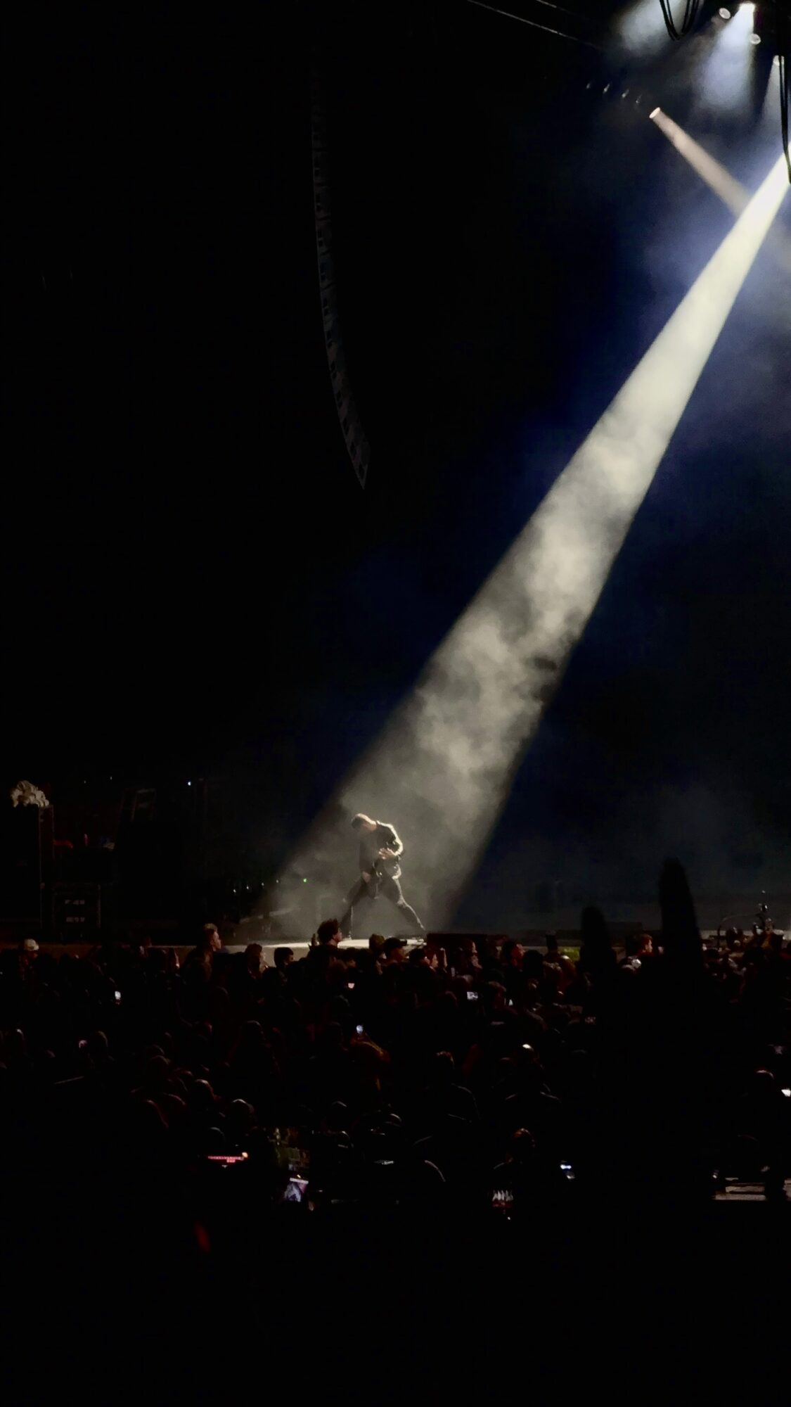 Stage with a performer illuminated by a bright spotlight, dark background, audience in foreground.