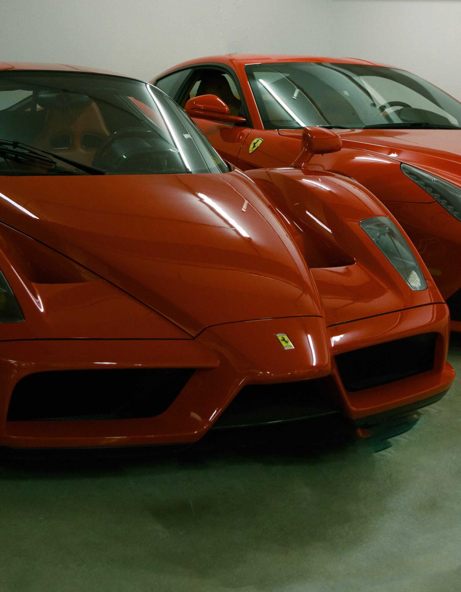 Two red sports cars parked side by side indoors, front view of the cars with sleek designs and low profiles.