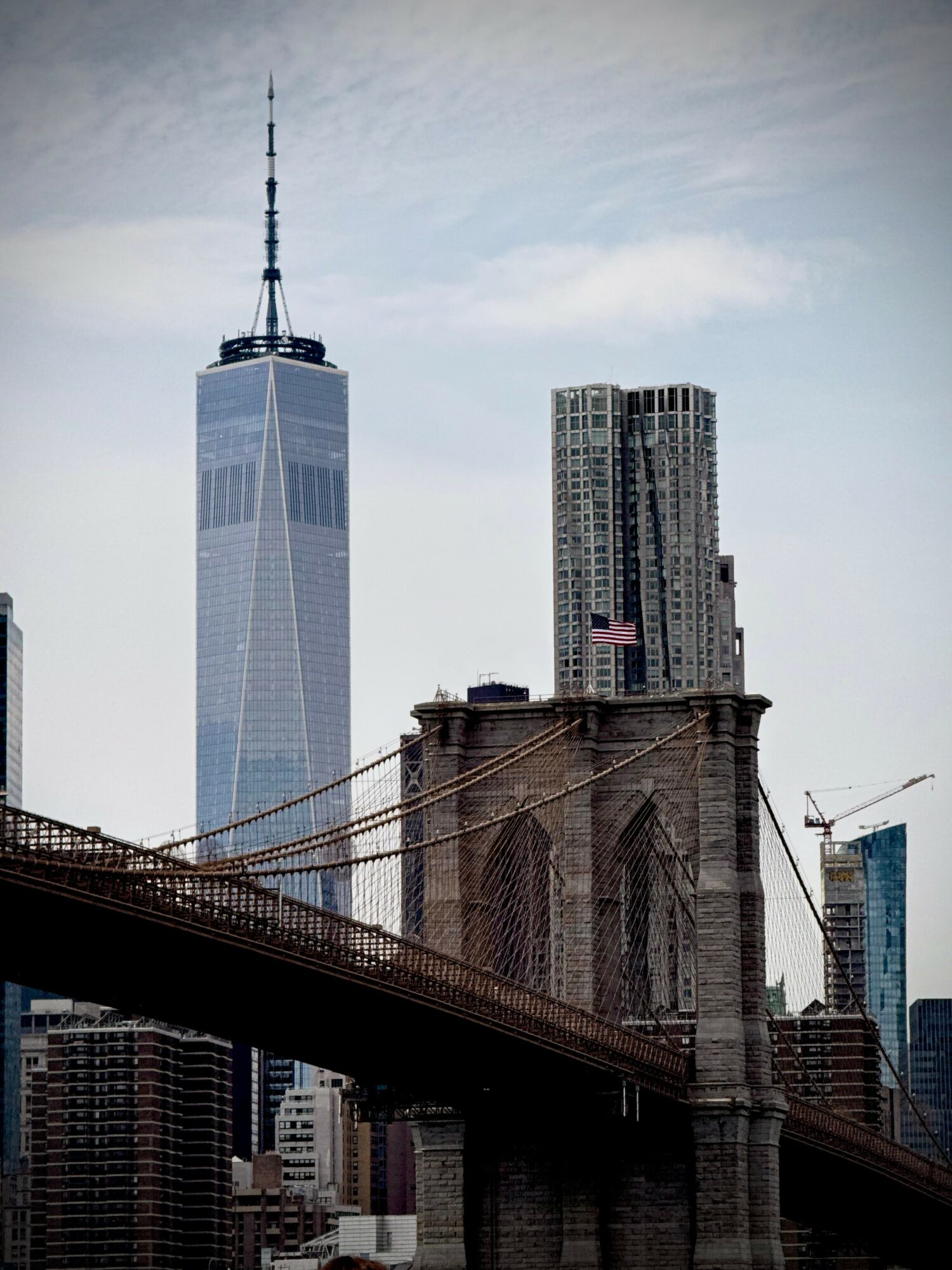 City skyline with tall skyscrapers, including One World Trade Center, and a bridge in the foreground.