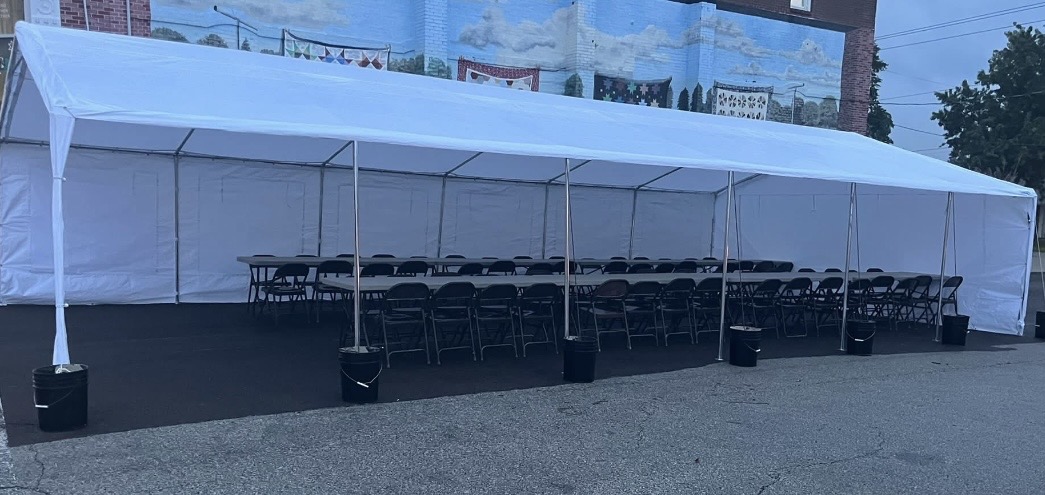 Long white tent with rows of chairs inside, set up outdoors on a paved surface.