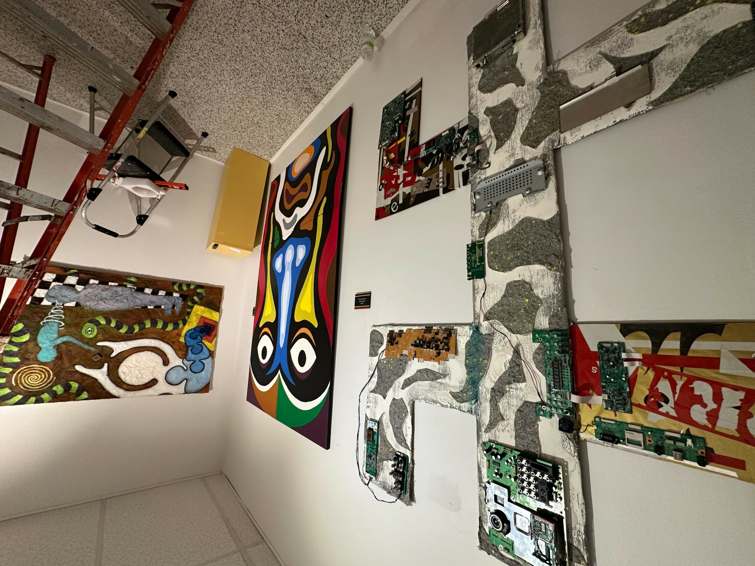 Gallery wall with colorful abstract paintings and mixed media art pieces displayed vertically.