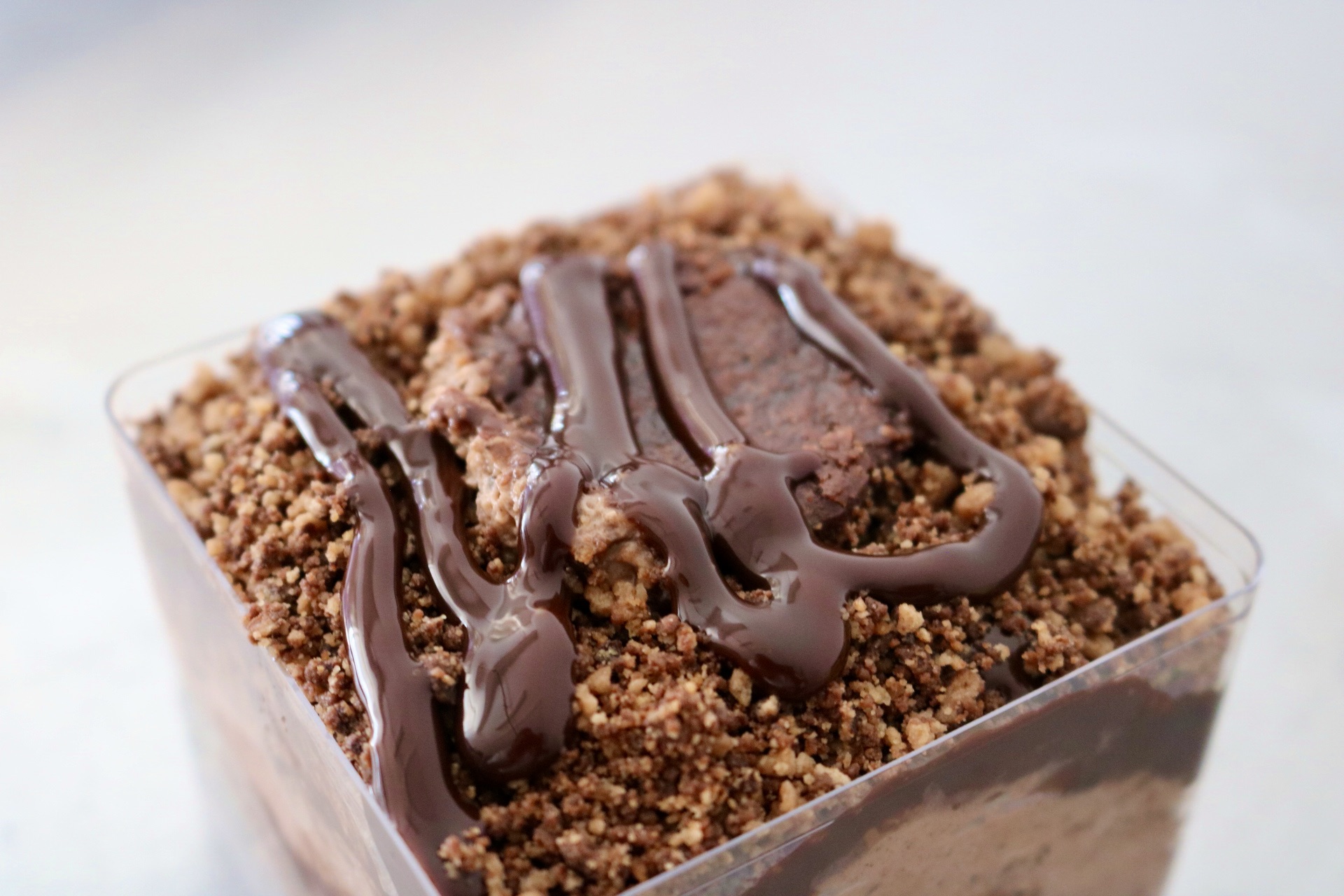 Chocolate dessert topped with crumbled cookie crumbs and drizzled with chocolate sauce in a clear container.