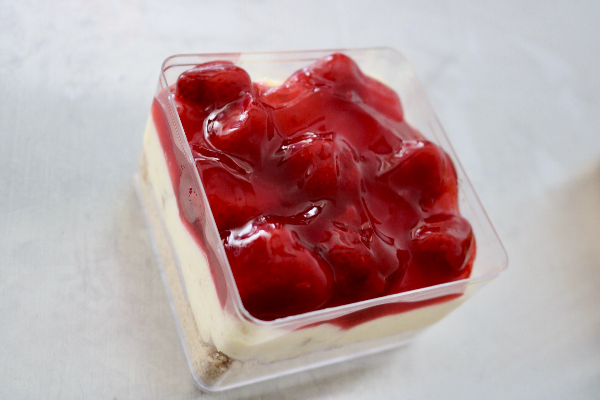 Square container filled with strawberries and red syrup on top, placed on a light surface.