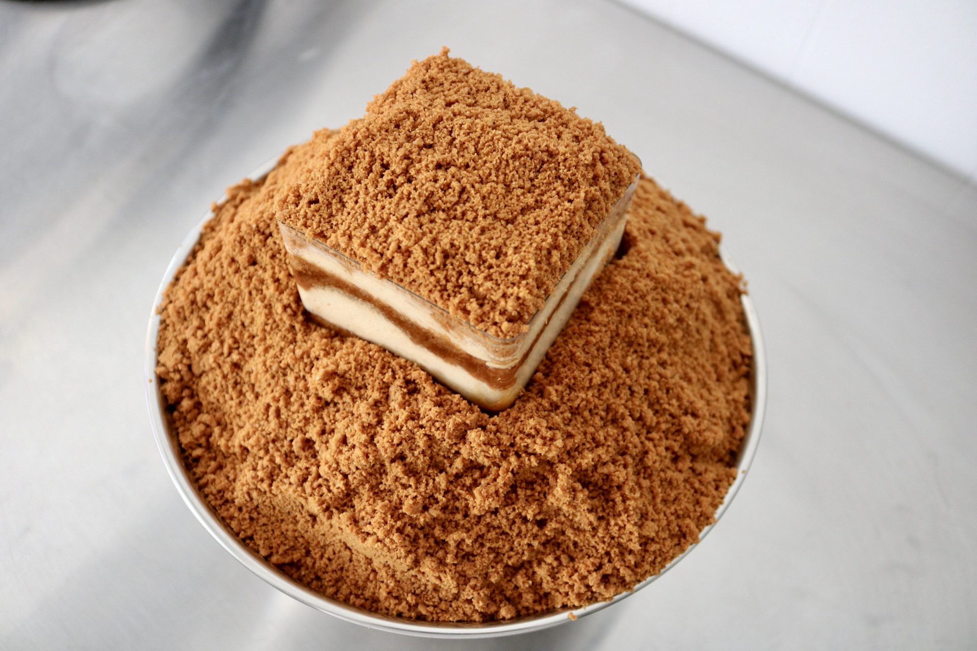 A layered dessert with a crumbly topping on a round plate, with a slice revealing cream filling inside.