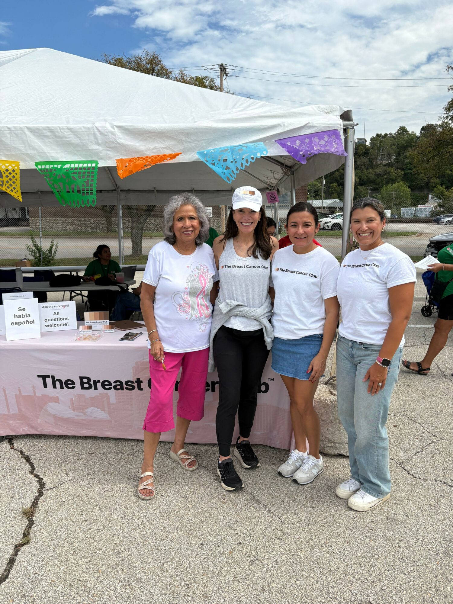 Group of women standing outdoors near a tent, with a banner reading 'The Breast' visible on the ground.