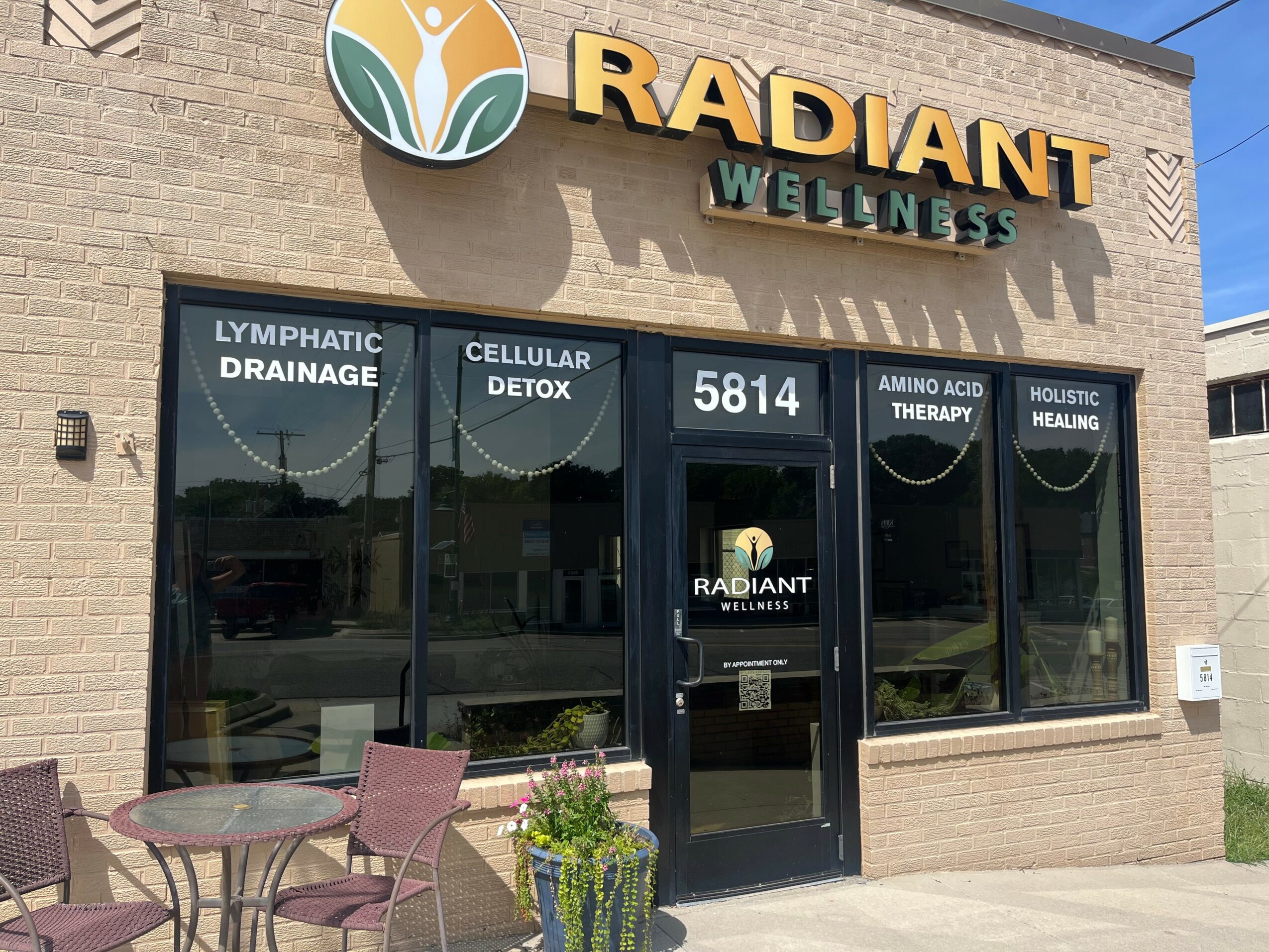 Storefront with large windows, sign reading 'Radiant Wellness,' and a door in the center. Window signs advertise health services.