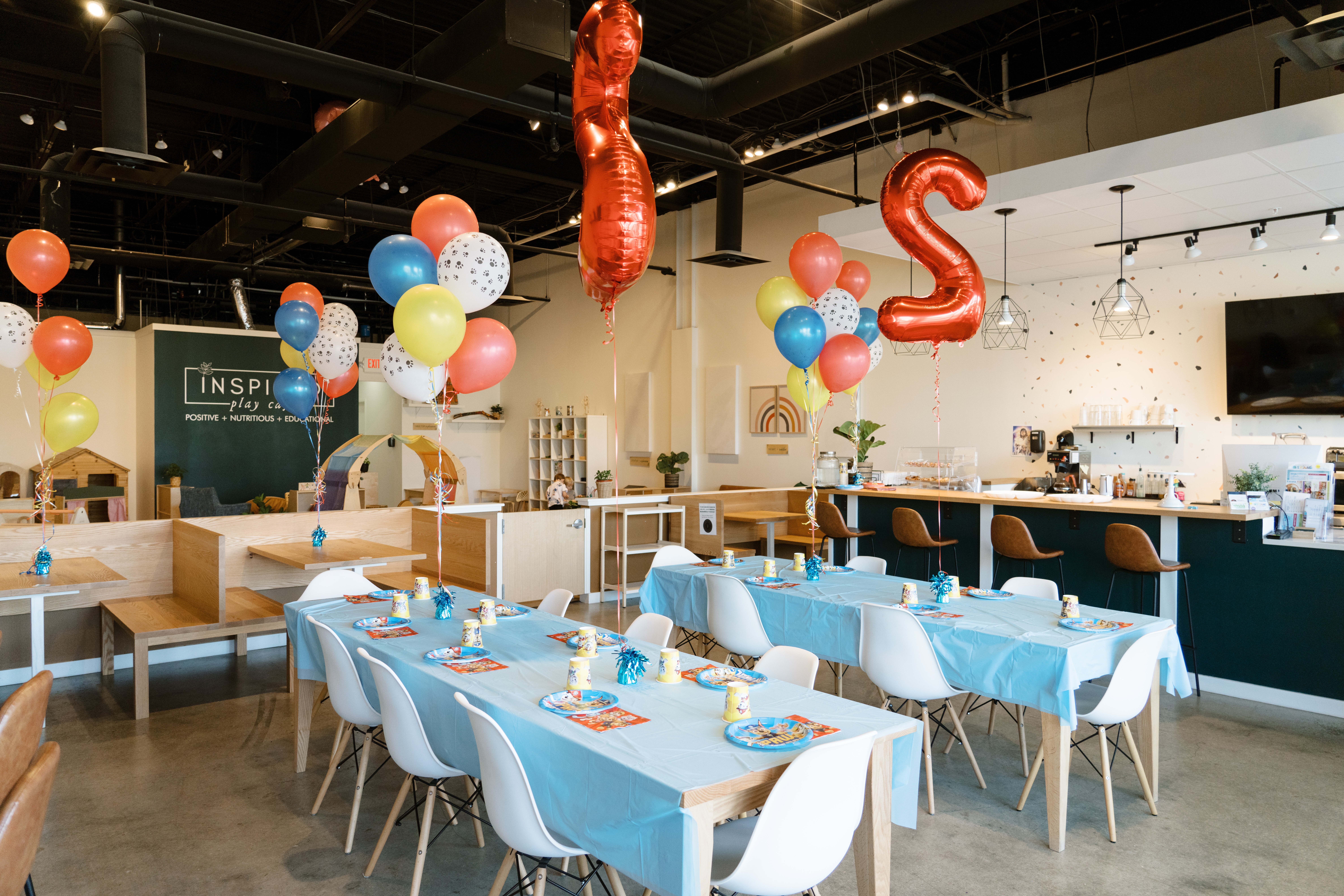 Party setup with balloons, tables, and chairs in a decorated indoor space, celebrating with colorful balloons and table settings.