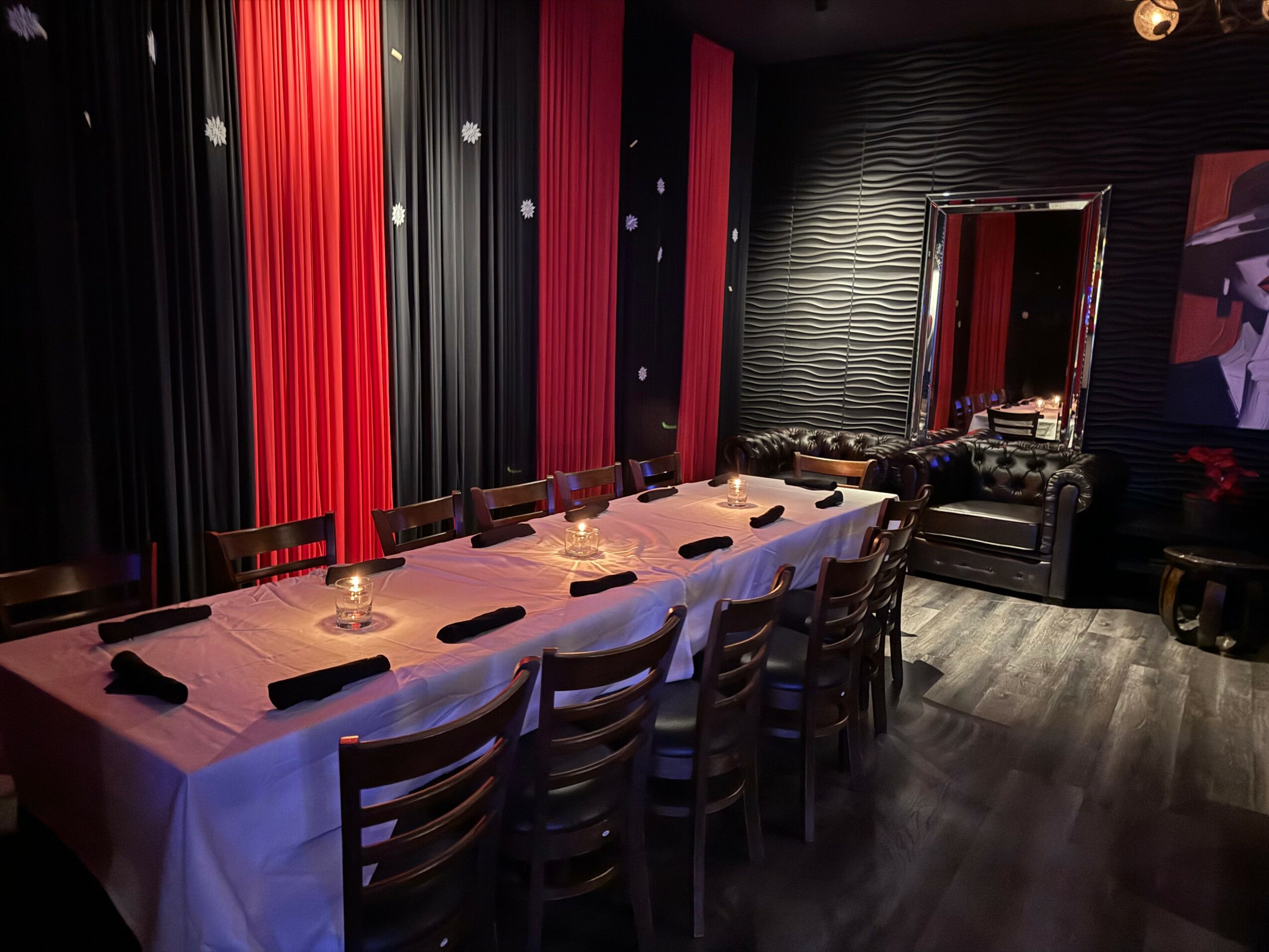 Long table with chairs in a dimly lit room, decorated with red and black curtains, and a mirror on the wall.