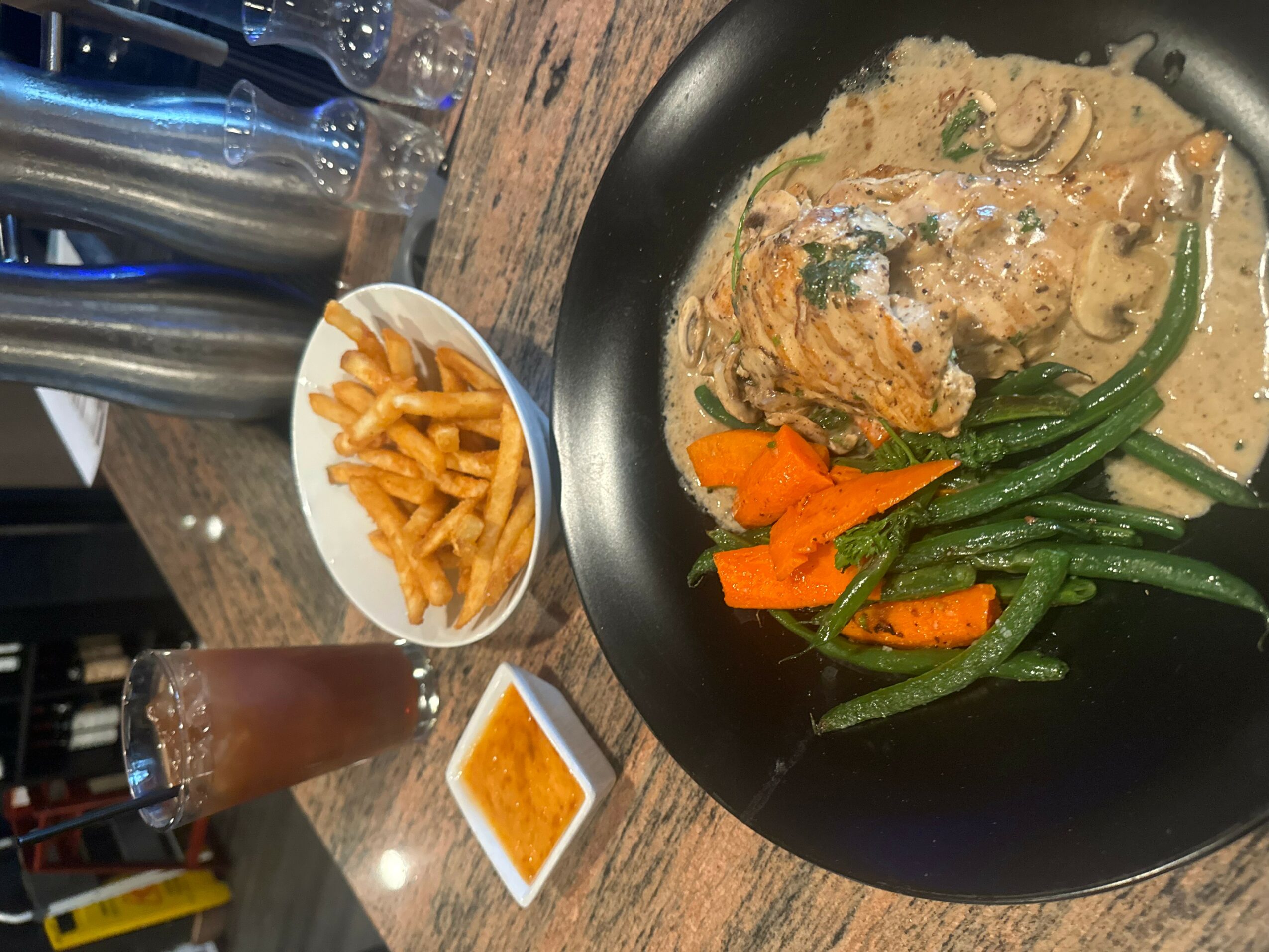 Plate with creamy dish, green beans, and carrots, alongside small bowls of pasta and sauce, on a wooden table.