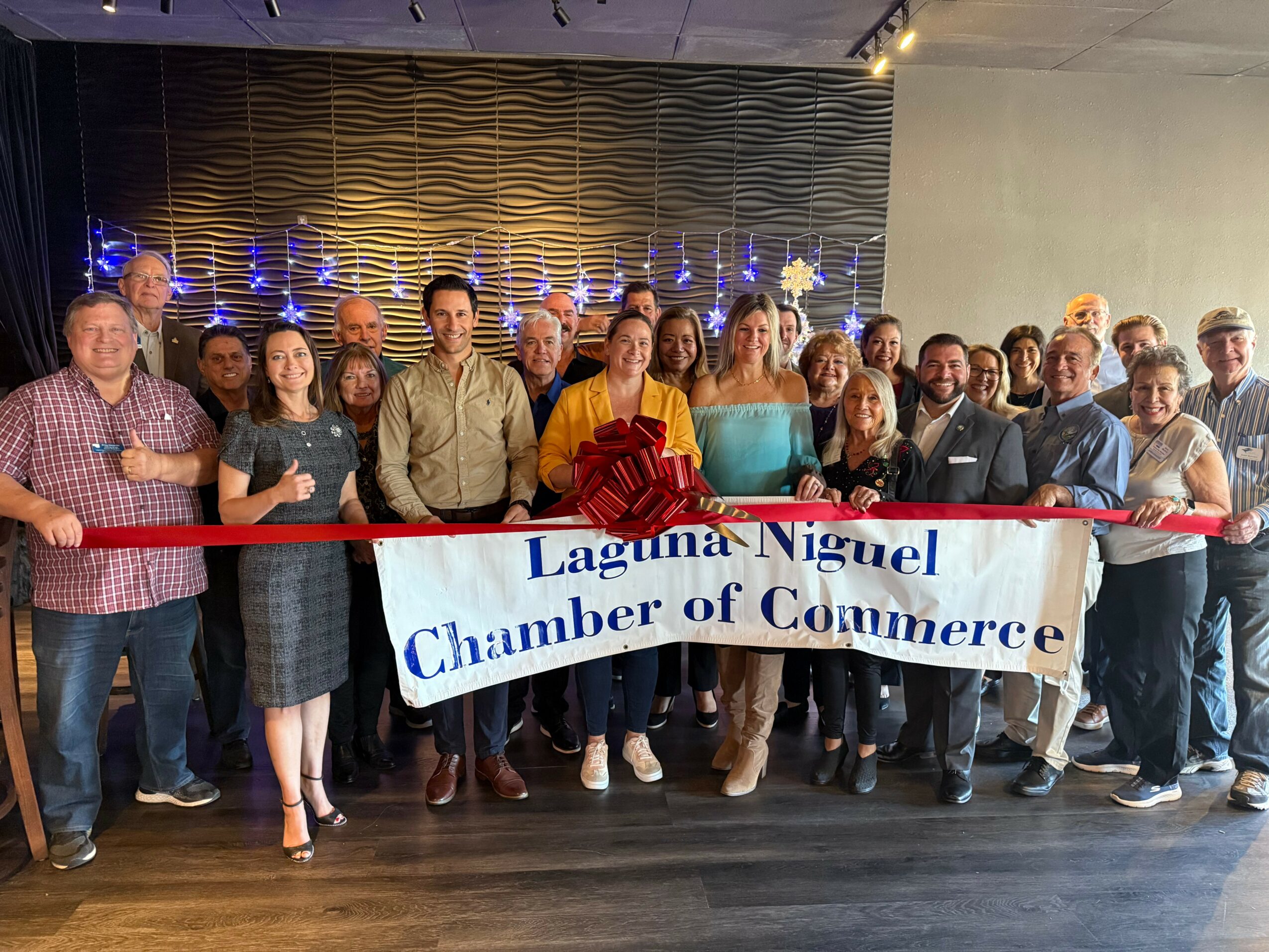 Group of people holding a banner that reads 'Laguna Niguel Chamber of Commerce' in a decorated indoor setting.