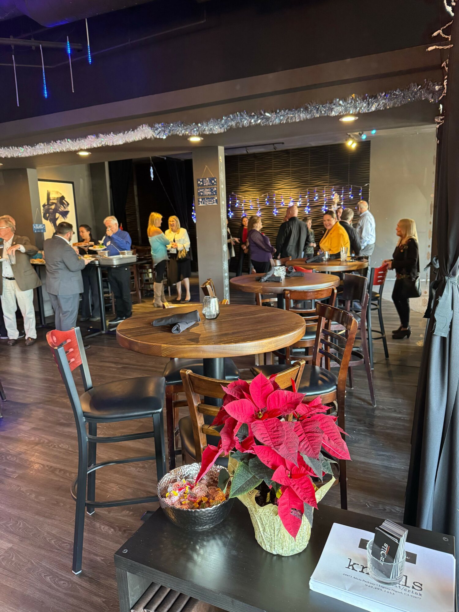 Table with poinsettia plant, glass, and papers, with people walking in the background at an indoor event.