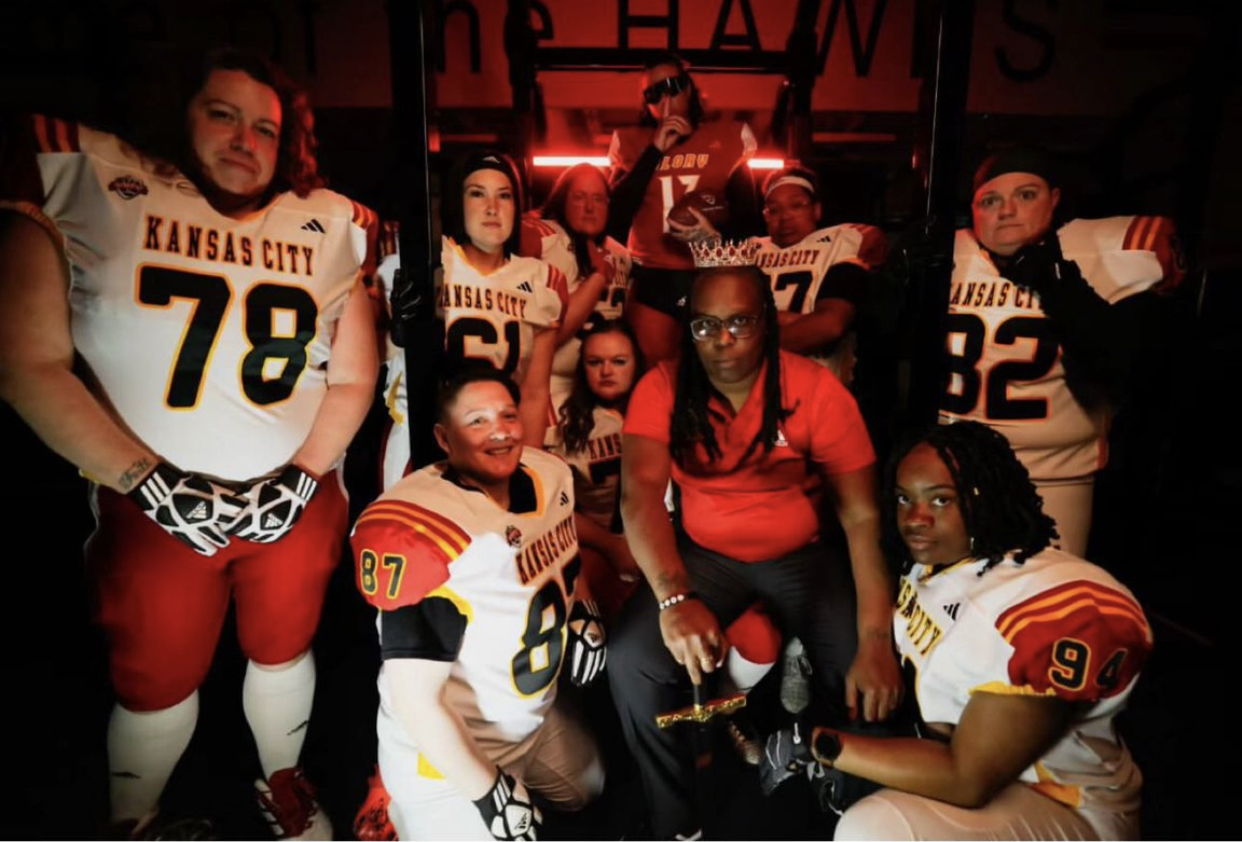 Group of football players and a coach in Kansas City jerseys, posing indoors with red lighting.