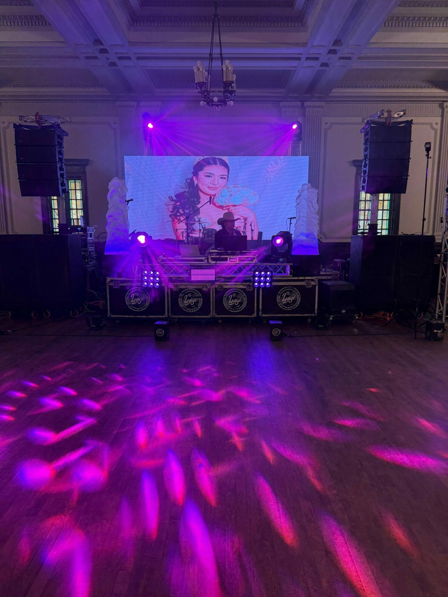 A DJ performs on stage with colorful lighting and a large screen displaying animated graphics behind them.
