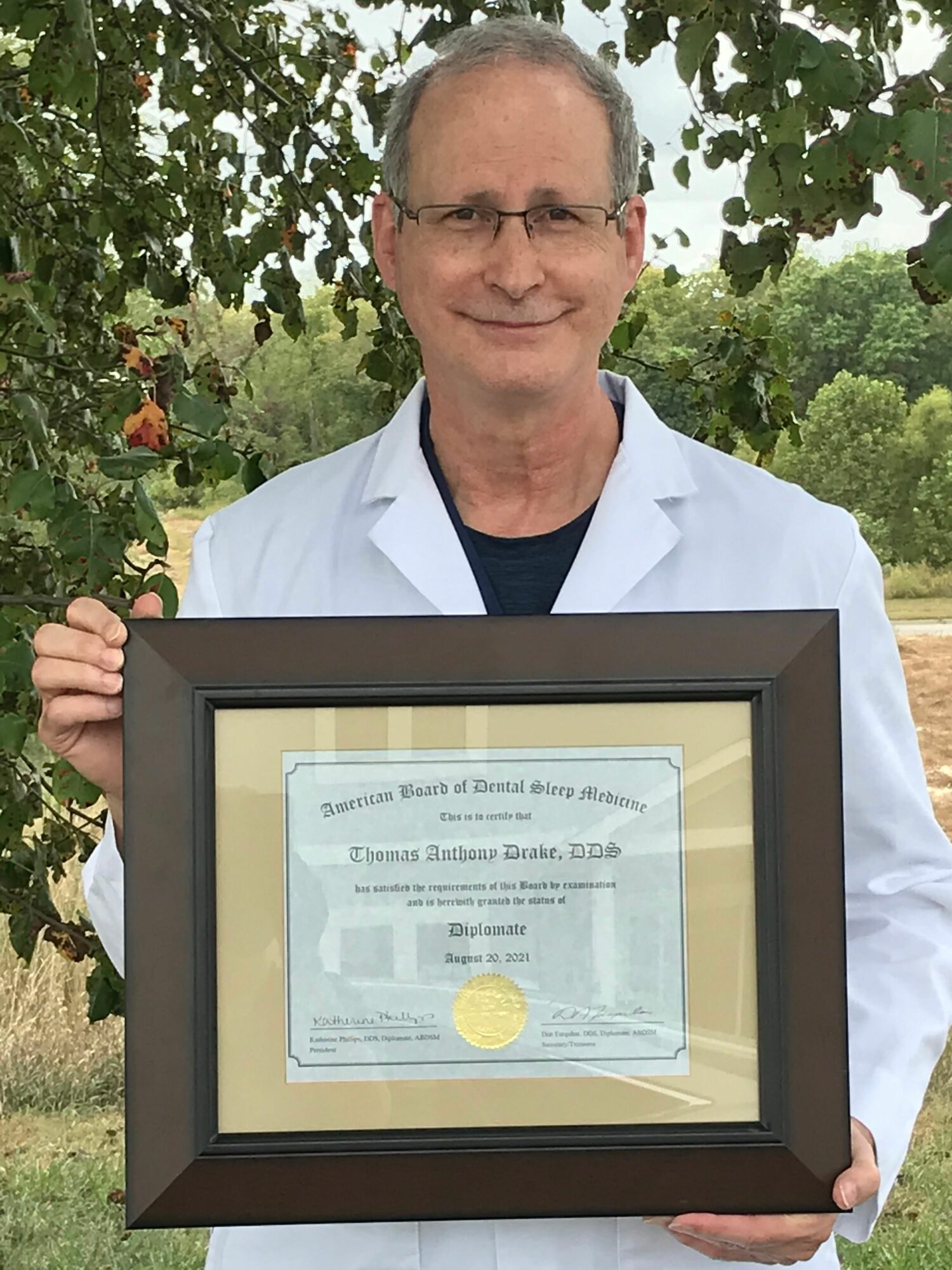 Person holding framed certificate outdoors with trees in background.